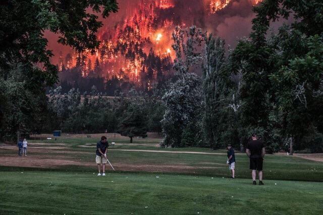 fires in the wild as people play golf in the background