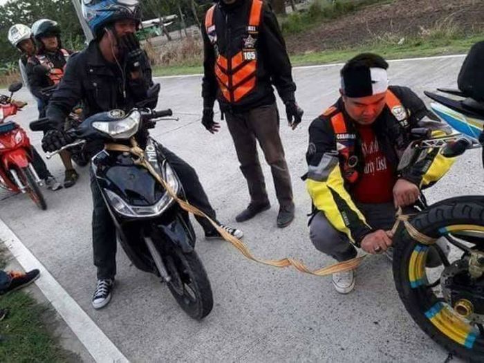 motorcycle wheel being attached to a scooter in what is clearly going to be a failed attempt to tow it