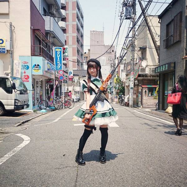 Japanese girl dressed in cosplay outfit of an anime girl and wit ha very large and robust looking rifle
