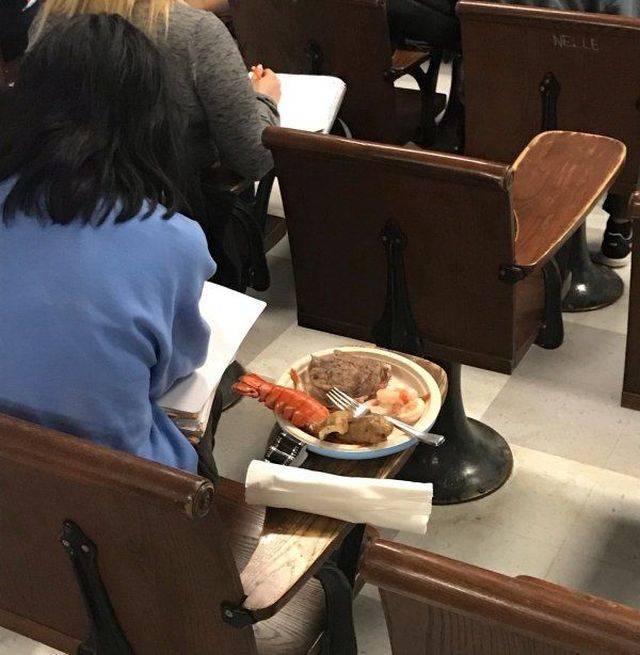 Student eating an elaborate meal in class including lobster and steak