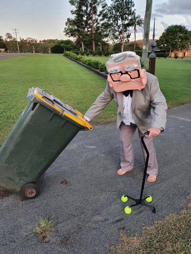 man dressed as carl from the pixar movie up taking out the trash