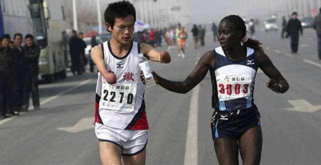 Woman handing a bottle of water to a fellow runner without hands.
