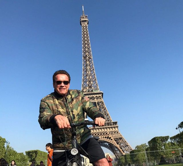 Arnold Schwarzenegger was riding a bike by the Eiffel Tower when he rode in front of a group of tourists trying to take a picture.