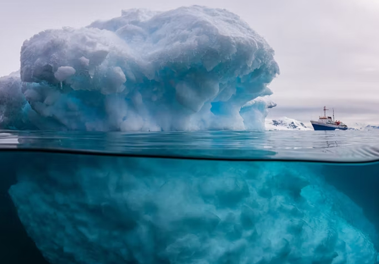 An astounding and massive iceberg that easily dwarfs the 3,000-tonne ship sitting nearby.
