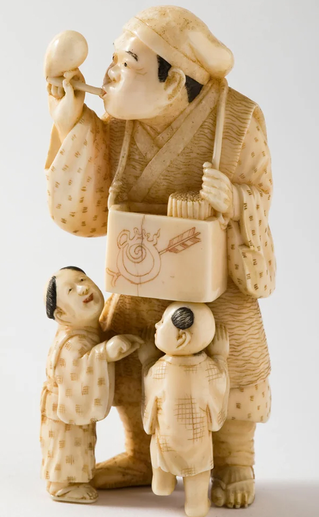 Ivory carving of a man blowing bubbles, and two children. Japan, 1870.