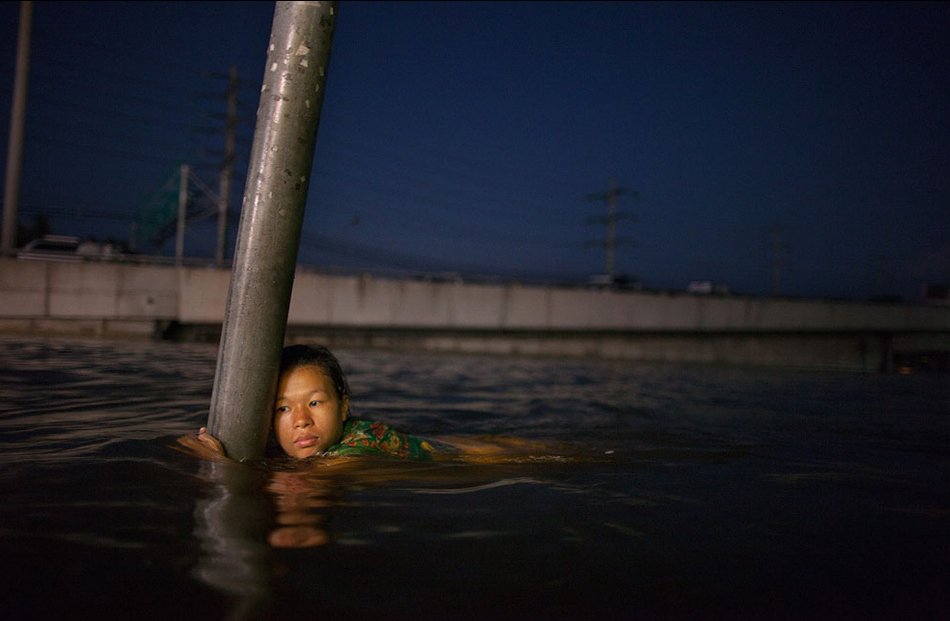 woman hangs onto a street sign in chest deep water along the flooded streets in Rangsit on the outskirts of Bangkok on October 24