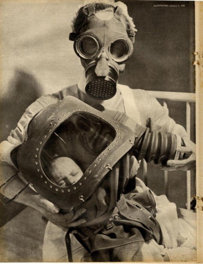 A nurse and a new born baby pose in their gas masks.
