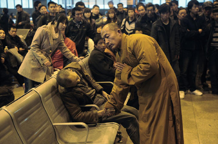 A monk prays over the body of an elderly stranger who died suddenly while waiting on a train in China.