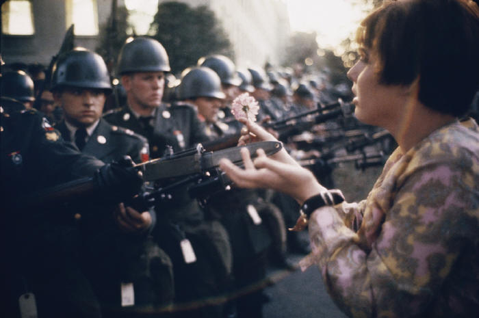 Jane Rose Kasmir plants a flower on the bayonets of guards at the Pentagon during a protest against the Vietnam War on October 21, 1967. The photograph would eventually become the symbol of the flower power movement.