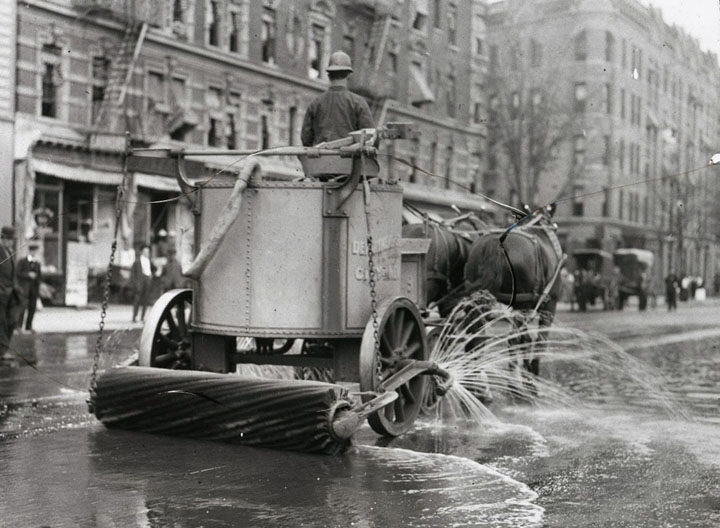 A two-horse team street cleaner, with sprayer, squeegee, and roller at rear.