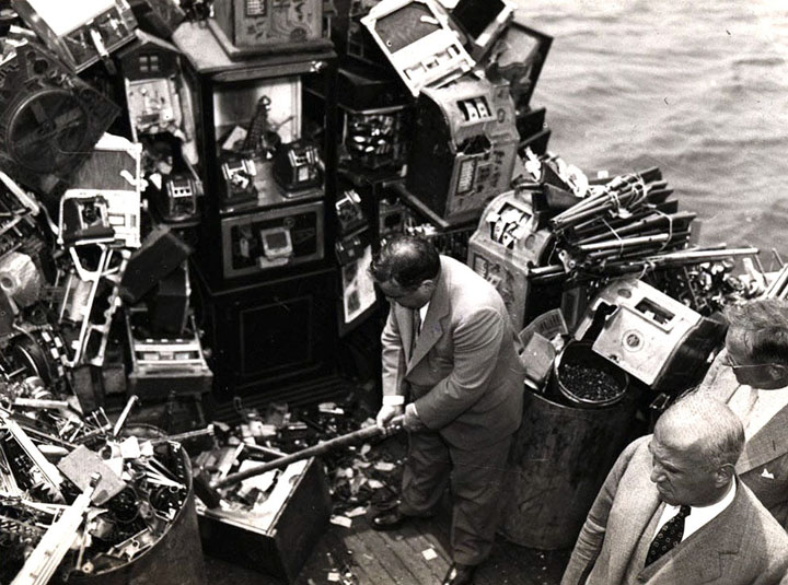 Aboard a police boat on October 10, 1934, New York Mayor Fiorello LaGuardia hacks away at confiscated slot machines about to be destroyed and dumped into New York harbor.