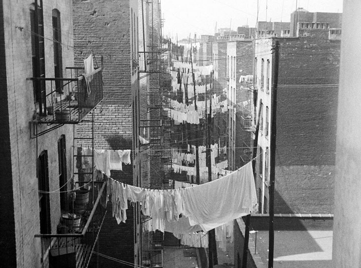 A view down an alley, as rows and rows of laundry hang from tenements ca. 1935-1941. Seen looking west from 70 Columbus Avenue or Amsterdam Avenue at 63nd Street.