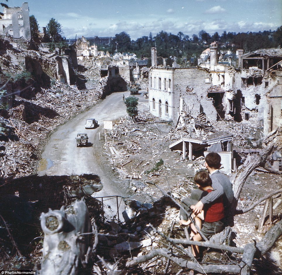 In the aftermath of the D-Day invasion, two boys watch from a hilltop as American soldiers drive through the town of St. Lo. France, 1944.