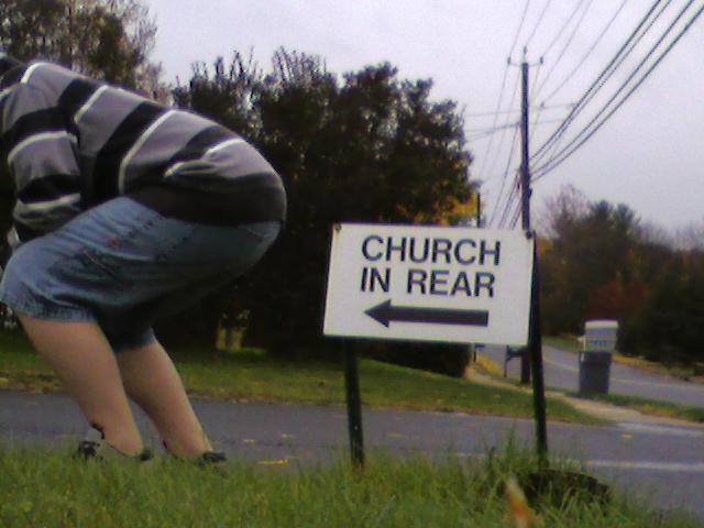 I sign by where I live pointing to a church hidden behind some trees and a friend of mine posing.