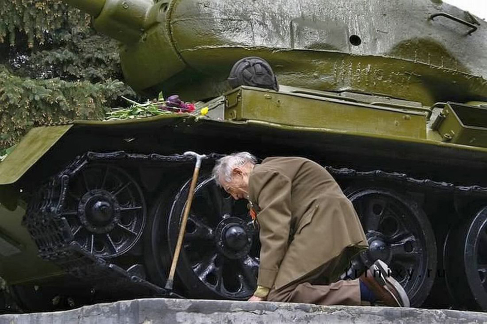 A Russian war veteran kneels beside the tank he spent the war in, now a monument.