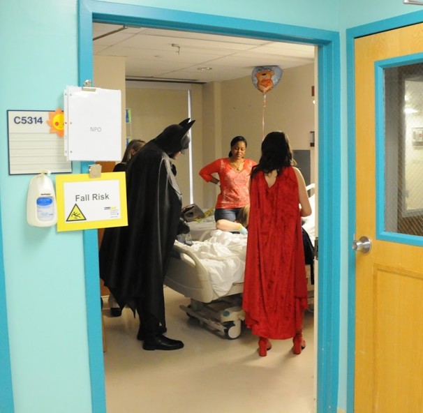 Batman and Wonder Woman being great people visiting a young female patient. Onions.