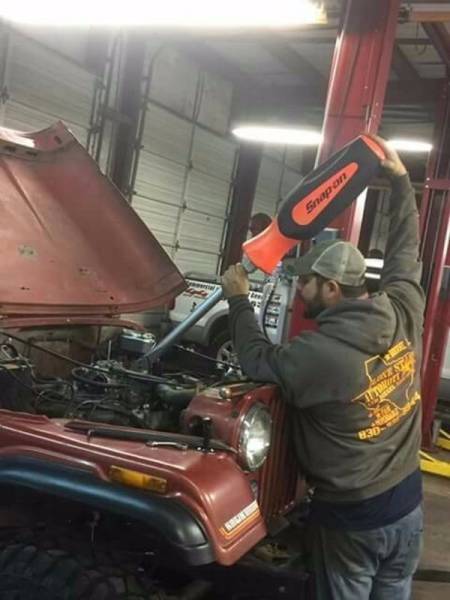 Man using comically large screwdriver to fix a Jeep