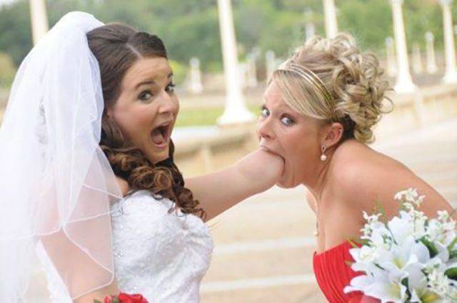 Funny bride picture of sticking her whole arm into a bridesmaid mouth.