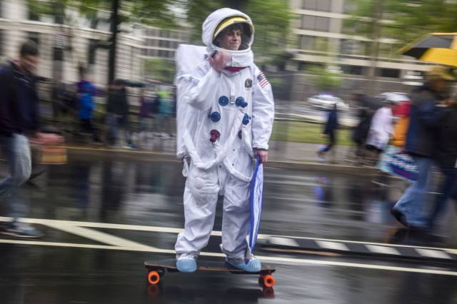 Man wearing a space suit skateboarding in the rain.