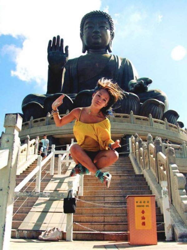 Awesome picture of woman in mid air in front of a Buddhist temple statue.
