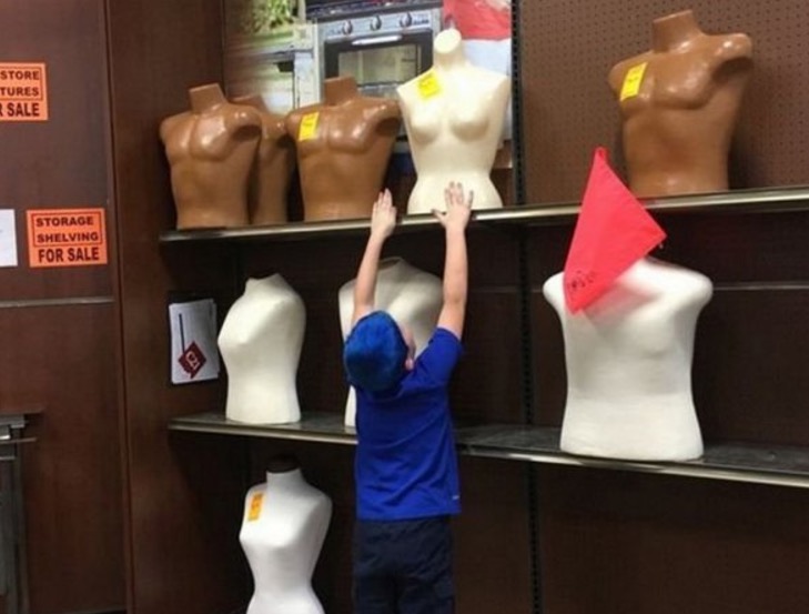 Funny picture of a kid trying to reach the mannequins boobs up top.