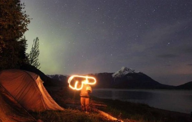 Person standing in the starlight by a beautiful lake and drawing a giant penis with a flashlight.
