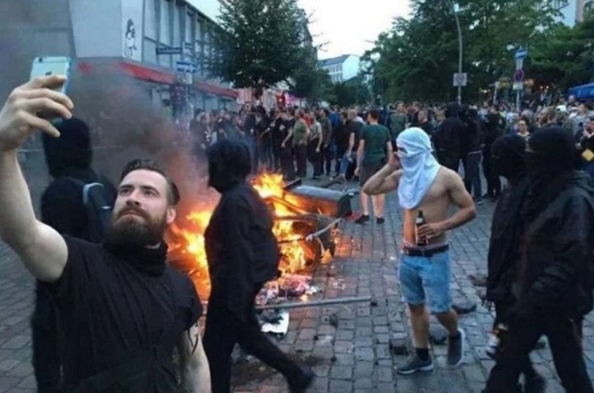 Man taking selfie as anarchy rages behind him.