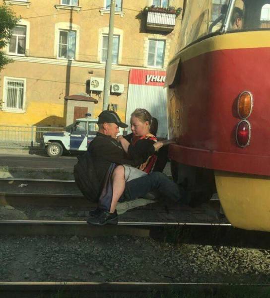 funny picture of couple that are attached to a train car and being dragged by it most likely to avoid paying the fare