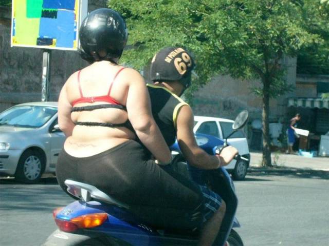 Very fat woman sitting on the back of a scooter.