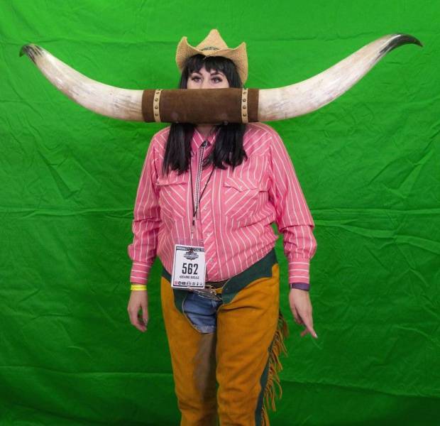 Woman dressed as a cowgirl and wearing large bull horns on her mouth.