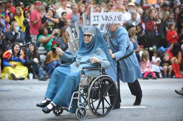 Woman in a wheelchair dressed as Lady Olenna with sign IT WAS ME behind her.
