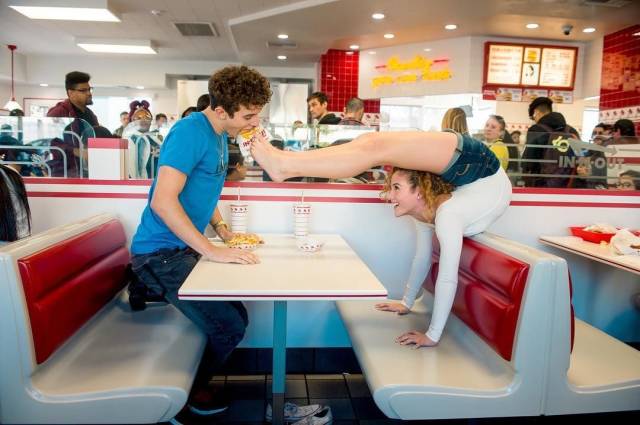1f4g6b8t5  woman using her feet in a fast food restaurant to feed the boy sitting across from her in her booth.