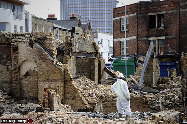 Charred Buildings in London - A workman stands guard beside the charred remains of the Reeves furniture shop.