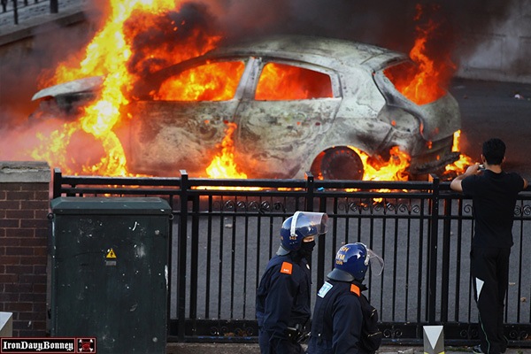Riots in Birmingham - Police walk past a burning car during riots in Birmingham City Centre.