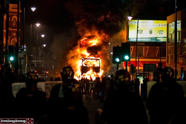 Double-Decker Bus Burning - A double-decker bus burns as riot police try to contain a large group of people.