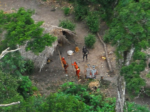 Taken from a small airplane, the photos show men outside thatched communal huts, necks craned upward, pointing bows toward the air in a remote corner of the Amazonian rainforest.