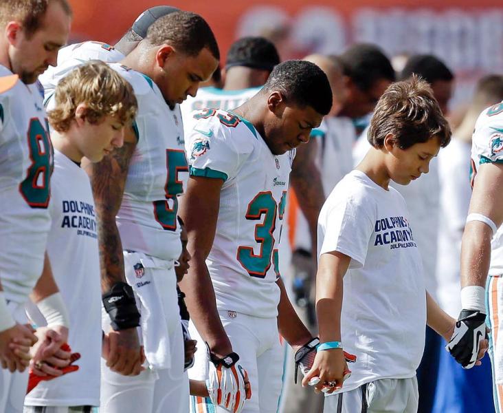 Miami Dolphins team members and young football players hold a moment of silence