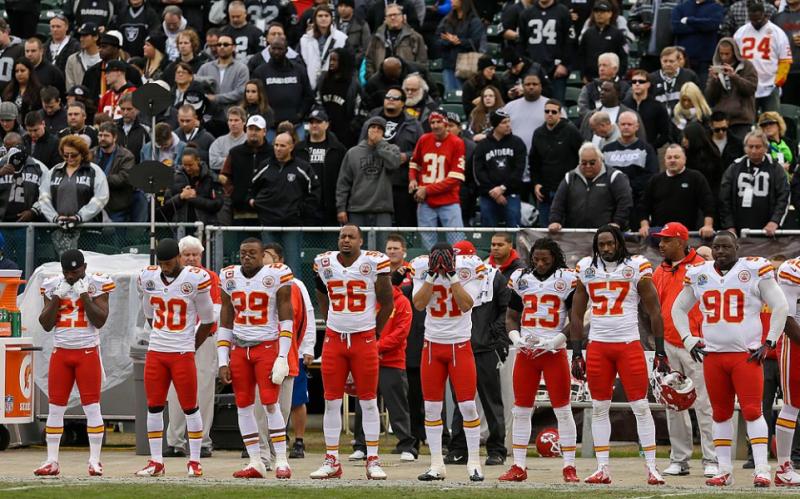 Kansas City Chiefs players and Oakland Raiders fans observe a moment of silence.