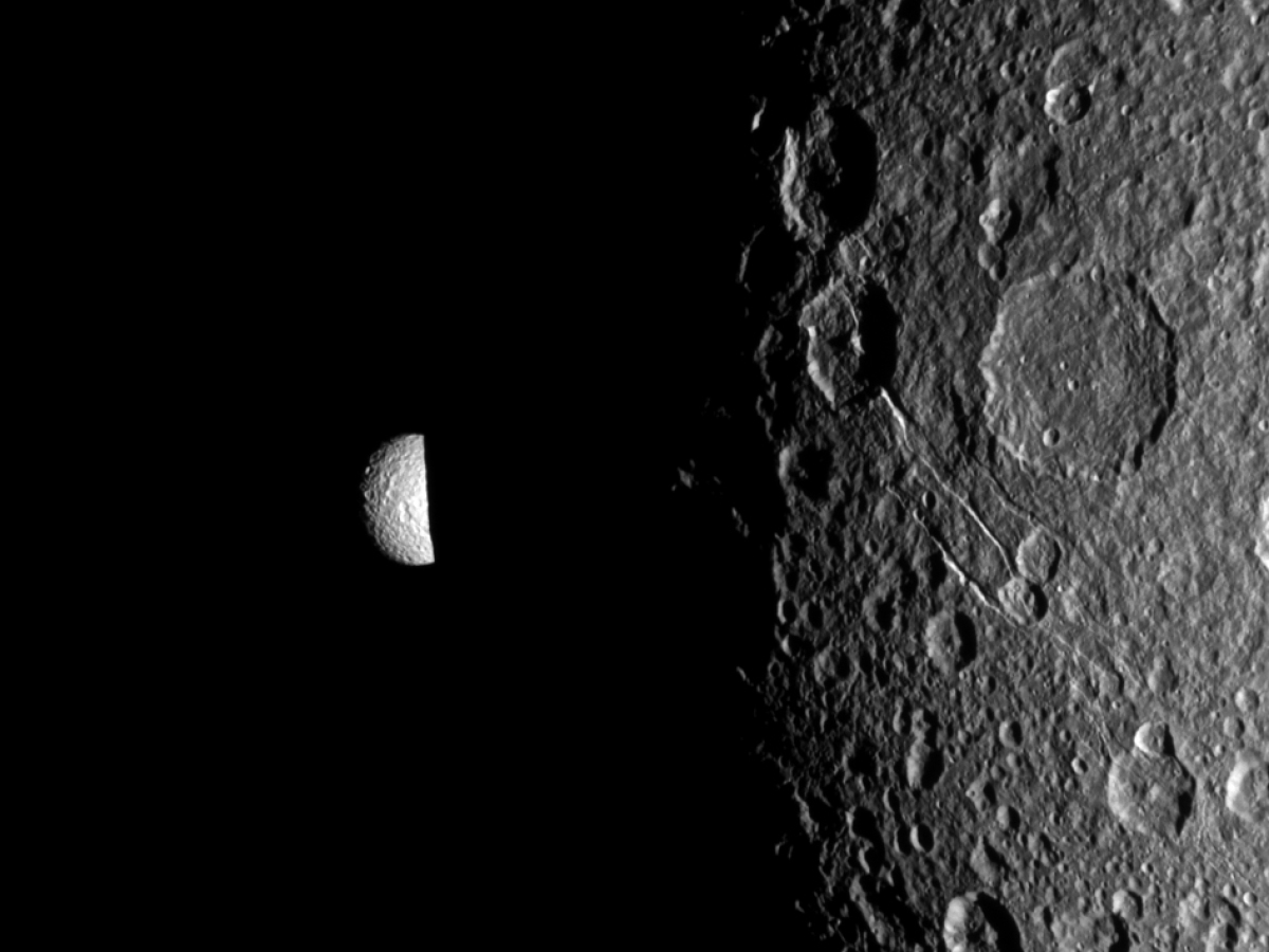 Saturn's moon Mimas peeks out from behind the night side of the larger moon Dione in this Cassini image.