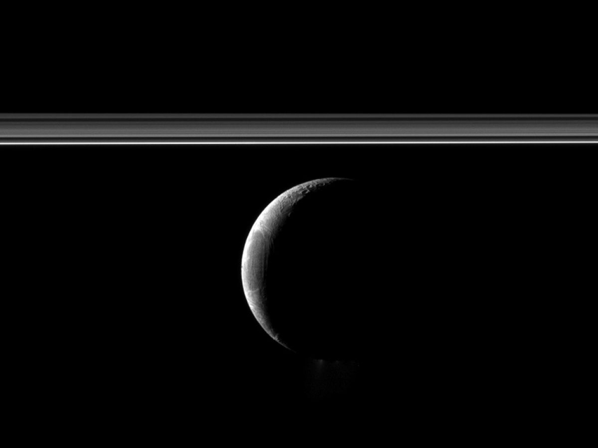 A crescent Enceladus appears with Saturn's rings in this Cassini spacecraft view of the moon.