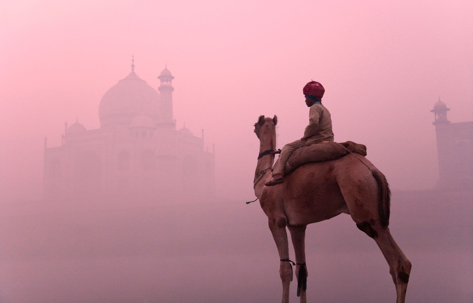 A boy rides on a camel in morning mist at the Taj Mahal in Agra, India.