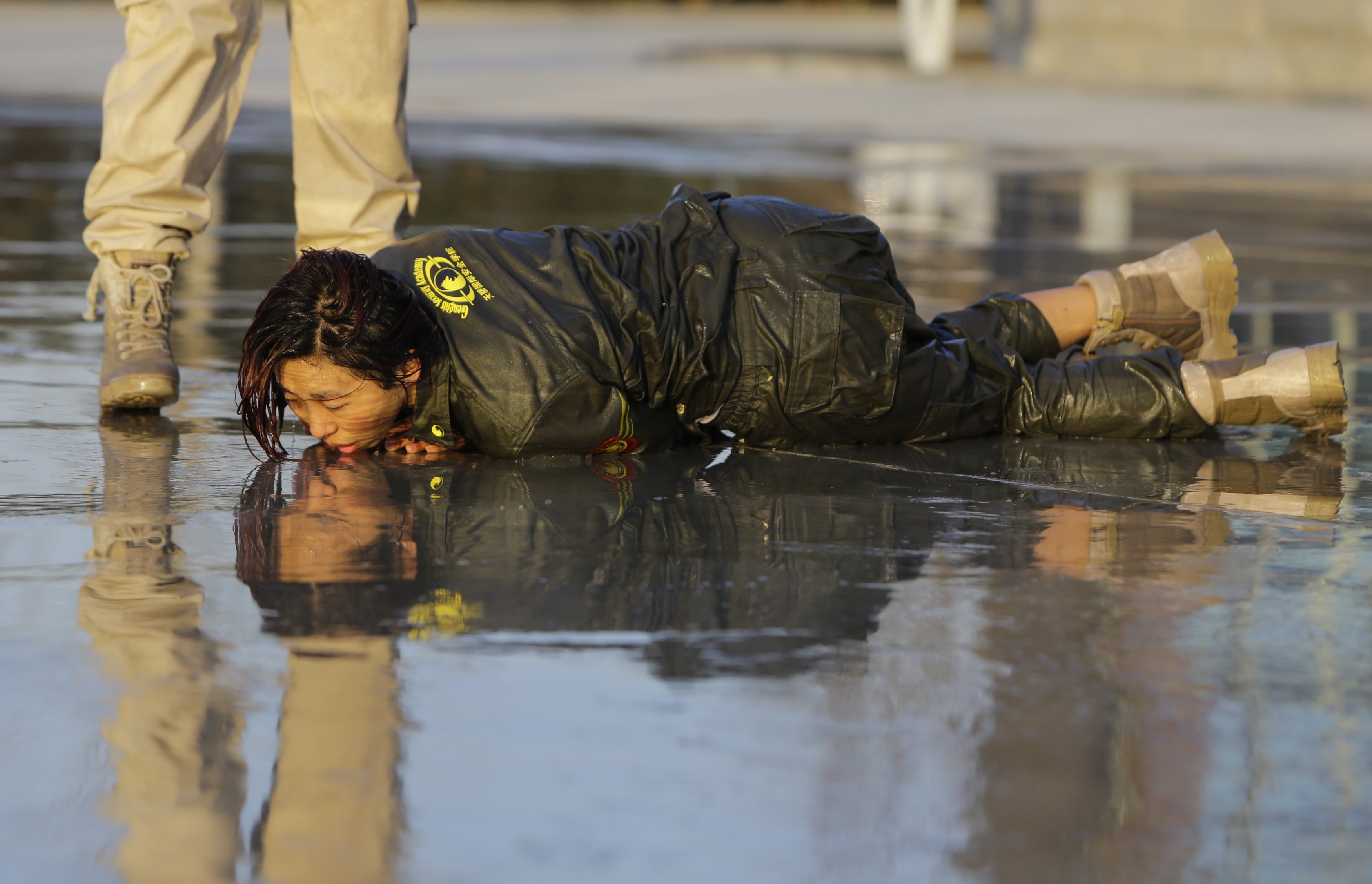 A female trainee lies on the ground after being drenched with water during Tianjiao Special Guard Security Consultant training.