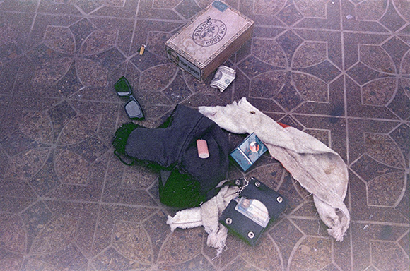 A cigarette lighter, a pack of cigarettes, a winter hat, cigarette butts, a wallet and sunglasses lie on the floor strewn around Cobain’s heroin kit.