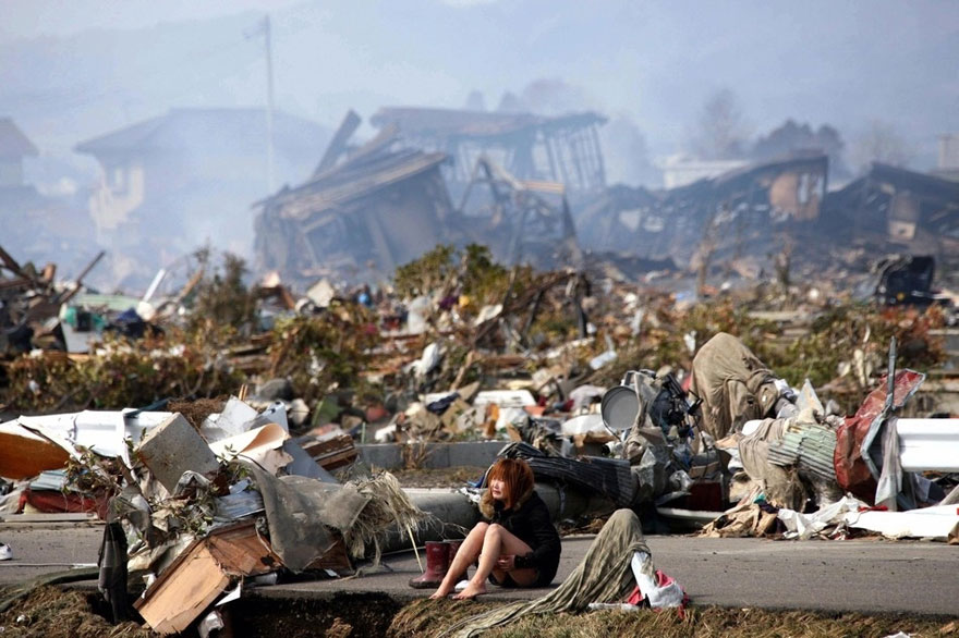 Woman sits among the wreckage caused by a massive earthquake and tsunami in Natori,Japan.