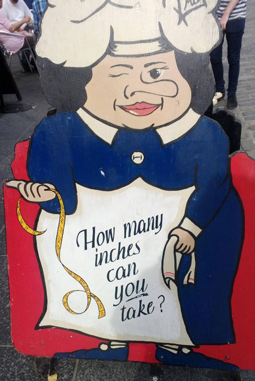 Cartoon cutout of a large woman chef, winking and asking how many 'inches can you take'