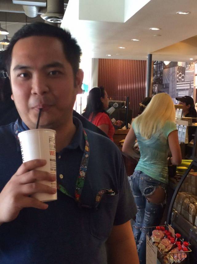 Funny picture of a dude drinking his coffee with a girl in the background with important part of her pants missing.