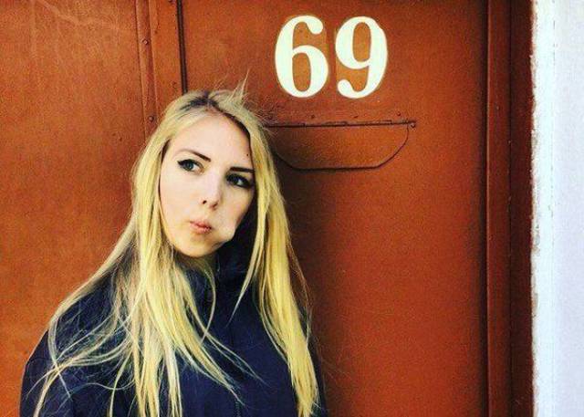 Girl making a BJ symbol with her mouth as she stands next to 69 house number