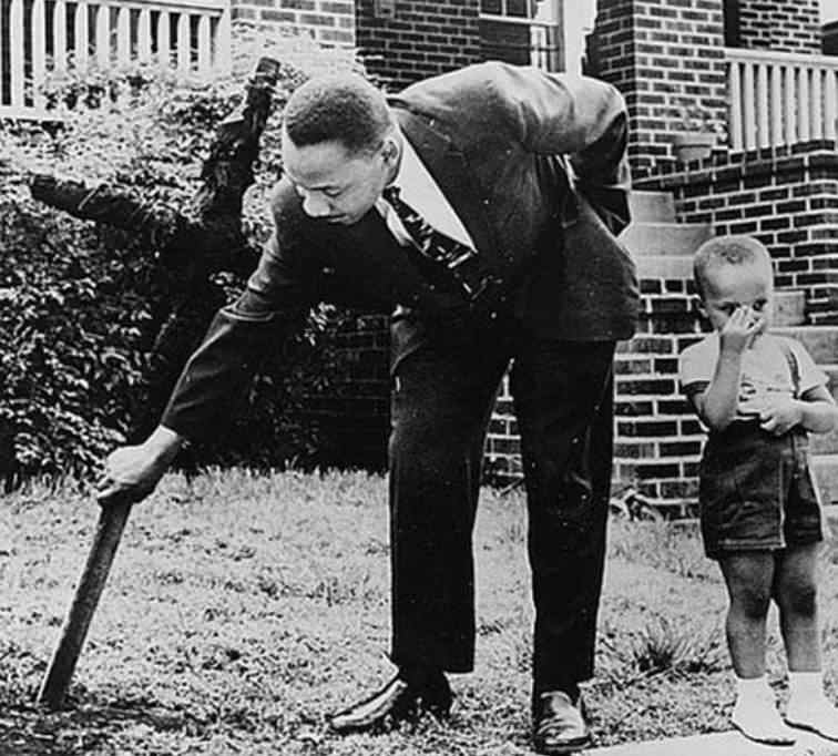 Martin Luther King Jr pulling a burnt cross out of the lawn outside his house while his son watched on