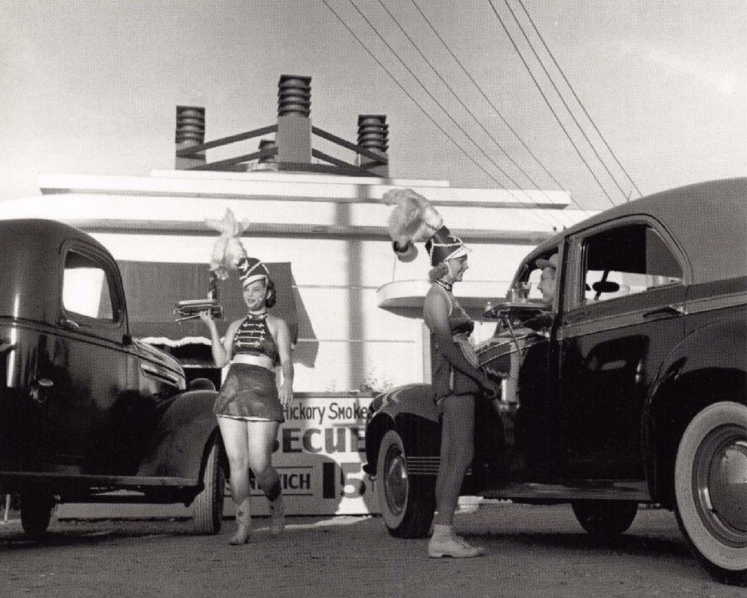 Waitresses known as CarHop girls deliver food to Drive-In patrons in Corpus Christi, Texas, USA in 1940. Known for their flattering outfits, especially showcasing their legs, CarHop girls were everywhere in the US in the 1940s-1950s. Sometimes they wore roller skates, and had uniforms that made them look like band members (as shown), cheerleaders, or sometimes even only wore bikinis at some locations, or any other absurdly sexy outfit to attract mostly male customers.