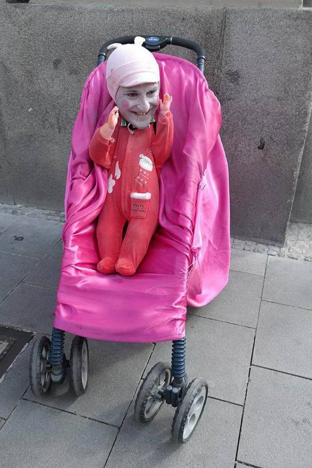 Weird picture of a grown mans face on a baby doll in a stroller on the street